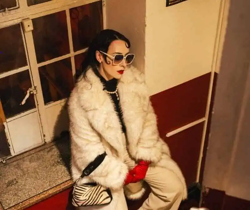 Stylish woman in faux fur coat with zebra print purse and bold accessories, exuding confidence and elegance at Divine Magazine.