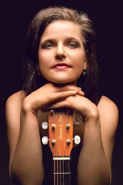 Confident woman with a guitar, expressing strength and passion in a studio setting.