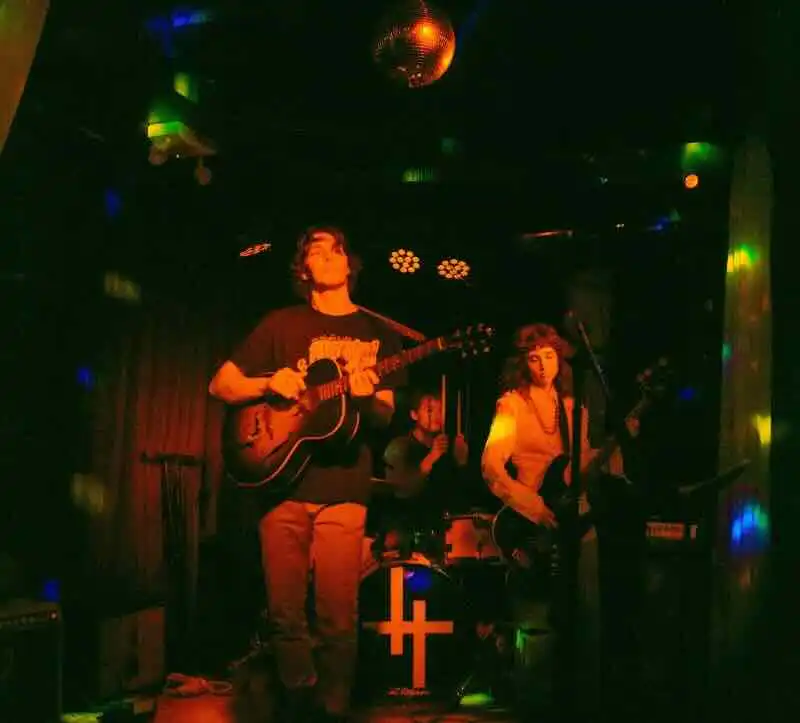 Live band performing with guitars and drums on stage under colorful lighting.