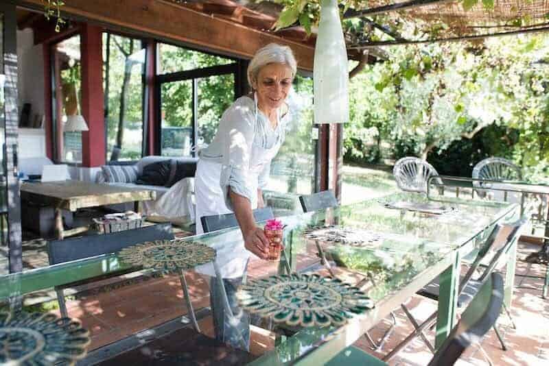 Beautiful senior woman setting a table outdoors in a lush garden.