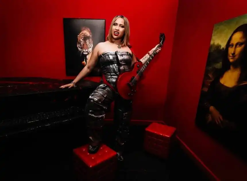 A woman with a guitar in a vibrant red-walled art studio, surrounded by iconic artwork including the Mona Lisa.