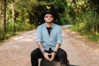 Individual with guitar case in a forested setting.