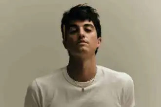 A confident young man with dark hair in a white t-shirt and beige pants, showcasing casual, modern fashion.