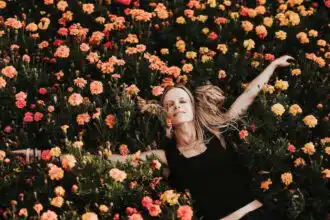 A woman lying peacefully in a vibrant bed of orange and yellow flowers, symbolizing freedom and renewal.
