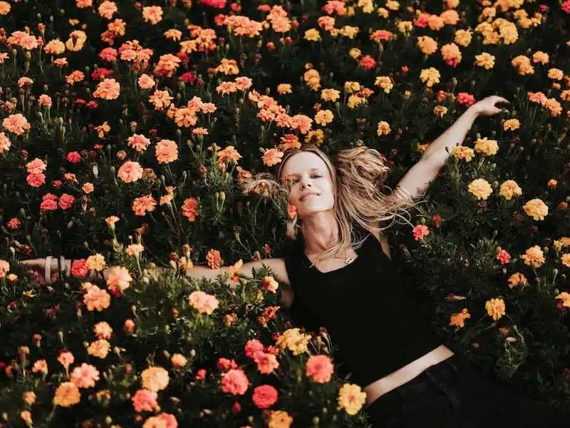 A woman lying peacefully in a vibrant bed of orange and yellow flowers, symbolizing freedom and renewal.