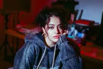 Woman with curly hair and casual hoodie in intimate indoor setting, showcasing contemporary fashion and lifestyle.