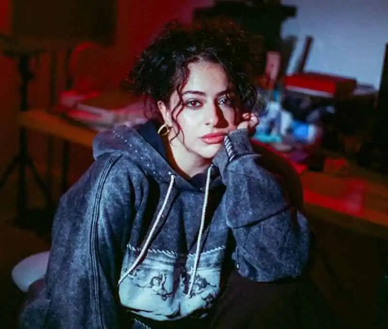 Woman with curly hair and casual hoodie in intimate indoor setting, showcasing contemporary fashion and lifestyle.