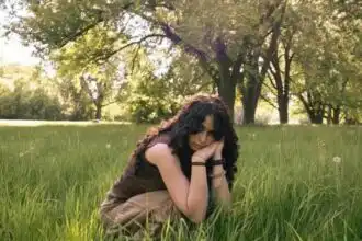 Young woman sitting peacefully in a grassy meadow with trees in the background.