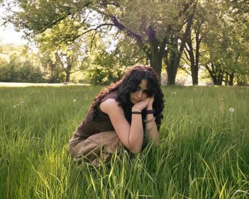 Young woman sitting peacefully in a grassy meadow with trees in the background.