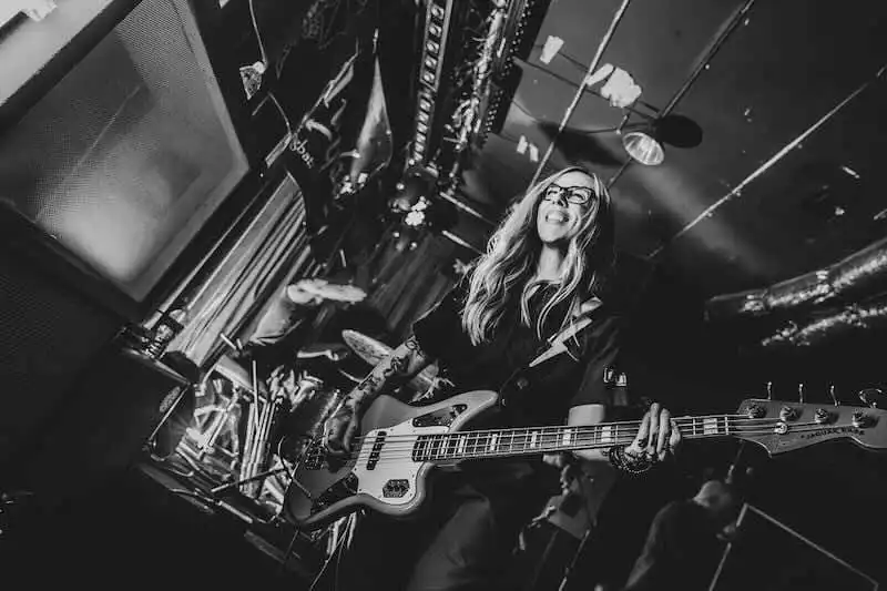 Vibrant woman playing bass guitar on stage during a lively concert at Divine Magazine event.