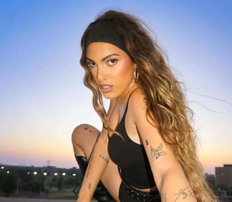 Vibrant woman with tattoos and confident pose during sunset with blue sky background.