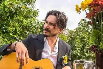 Outdoor garden scene with man playing guitar, surrounded by colorful flowers and lush greenery.