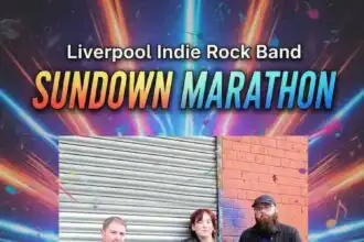 Alt text: A band of four young adults posing outdoors in casual attire against a metal and brick wall.