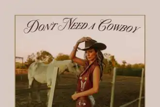 A woman in western attire and cowboy hat stands confidently near a horse in a rural setting, embodying country charm and cowboy spirit.