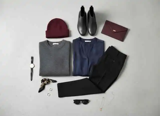 a flat lay of minimalist clothing in black, navy, grey, with burgundy and gold accessories