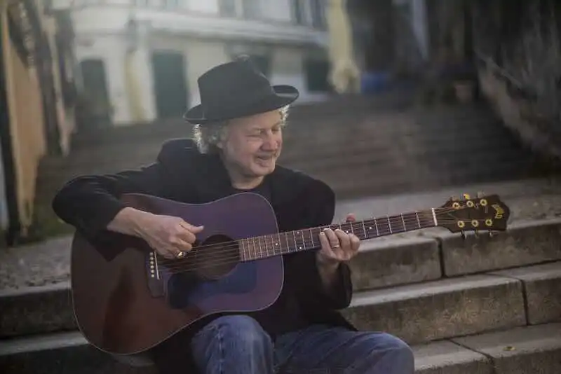 A man wearing a hat plays an acoustic guitar on city steps, capturing a moment of musical relaxation in an urban setting.