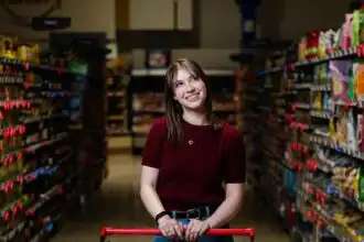 Happy woman smiling while shopping in grocery store aisle with cart.