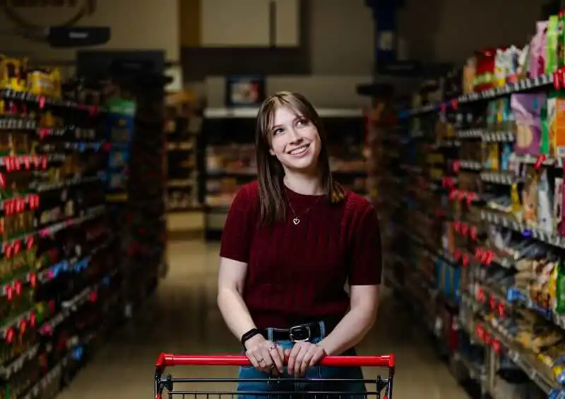 Happy woman smiling while shopping in grocery store aisle with cart.