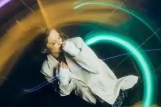 A woman with curly hair surrounded by colorful neon light trails, creating a dreamy, abstract effect. Perfect for articles on modern nightlife, art, or creative photography.