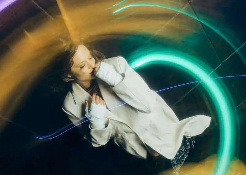 A woman with curly hair surrounded by colorful neon light trails, creating a dreamy, abstract effect. Perfect for articles on modern nightlife, art, or creative photography.