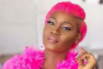 A confident woman with vibrant pink hair and matching feathered coat, showcasing bold style and self-expression.