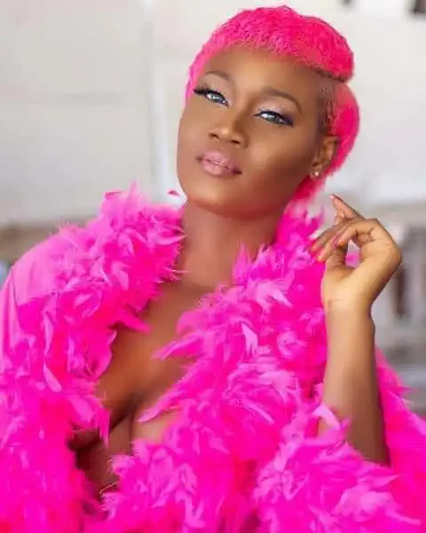 A confident woman with vibrant pink hair and matching feathered coat, showcasing bold style and self-expression.