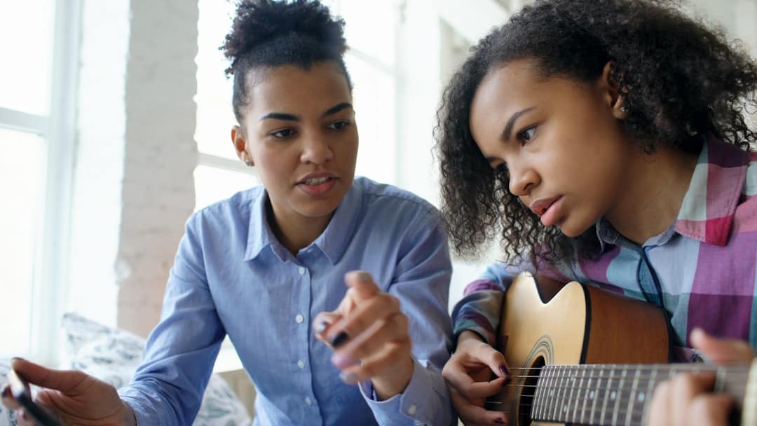 Two young women learning to play guitar together.