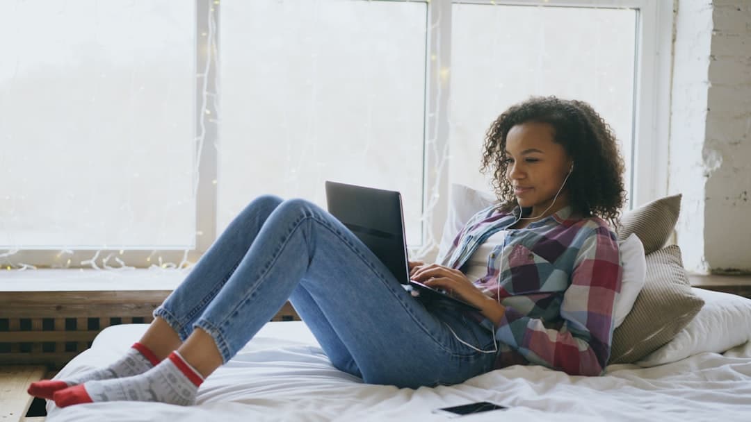 Young woman with headphones using laptop on bed