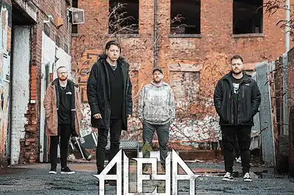 ALEYA band members standing outdoors in an urban alley with brick walls.