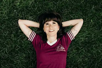 Ellie Heath lying on grass with arms behind head, smiling.