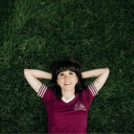 Ellie Heath lying on grass with arms behind head, smiling.