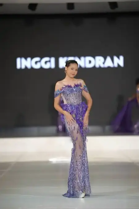 Elegant model in purple evening gown walking on runway during fashion show.