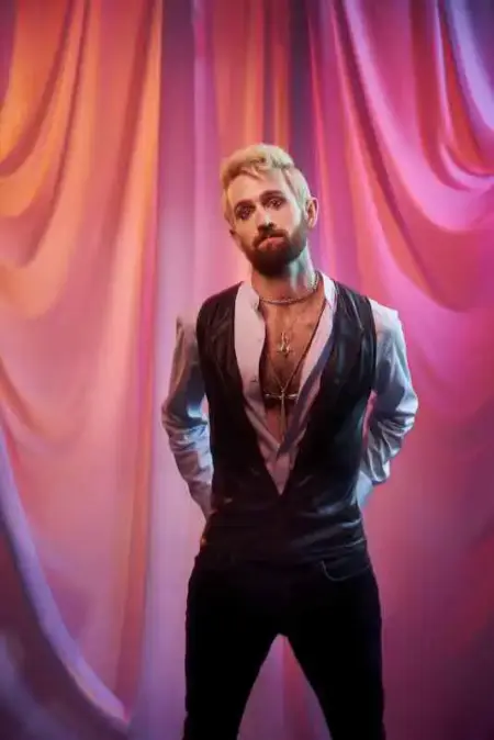 Horologica – Feather Single & I Want It More Than Anyone EP Male artist with a beard and styled hair standing in front of colorful draped curtains.
