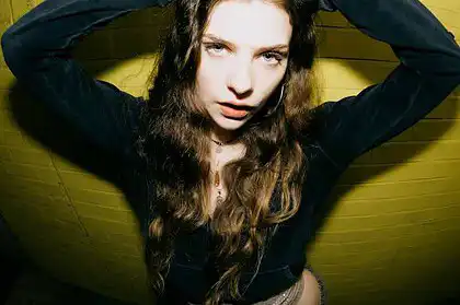 Lula Gold posing confidently against a yellow wall, promoting her new single "Wrong Lane".