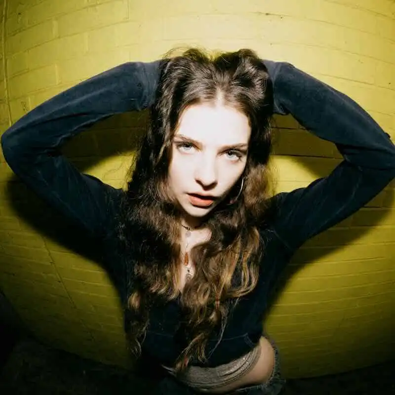 Lula Gold posing confidently against a yellow wall, promoting her new single "Wrong Lane".