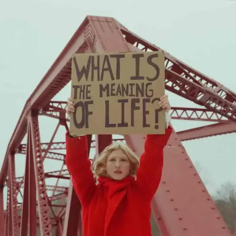 Meg Elsier – meaning of life (New Single) Woman holding a sign asking "What is the meaning of life?" under a bridge.