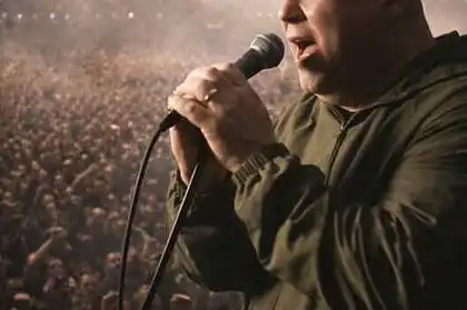 Mick Rochford singing into a microphone during a concert with a large audience.