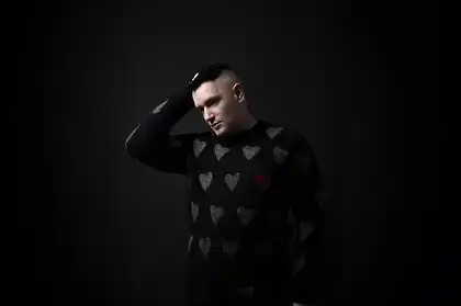 Portrait of Andrew Spice wearing a heart-patterned sweater against a dark background.