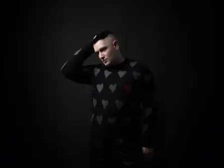 Portrait of Andrew Spice wearing a heart-patterned sweater against a dark background.