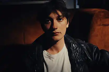 Portrait of YONAH, indie-rock artist, in a dark setting with leather jacket.