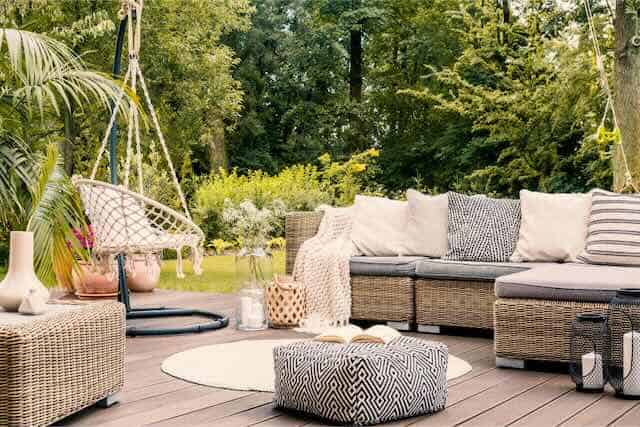 Stylish outdoor seating area with wicker sofa and hanging swing chair in garden setting.