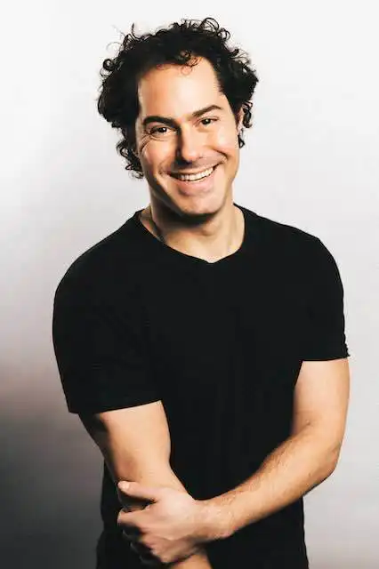 Smiling man with curly hair wearing a black T-shirt, expressing happiness and confidence.