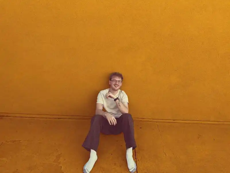 Happy man sitting on colorful wall, showcasing LGBTQ+ pride, positivity, and personal style.