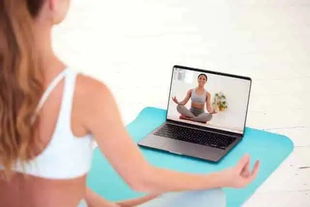 Woman practicing yoga and meditation during an online session, focusing on mindfulness and relaxation.