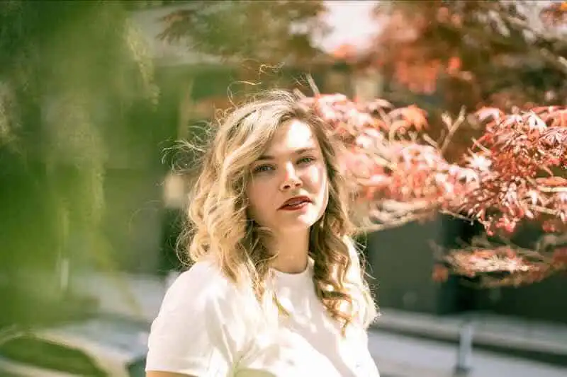 Beautiful woman standing amidst vibrant autumn leaves in a serene outdoor setting.