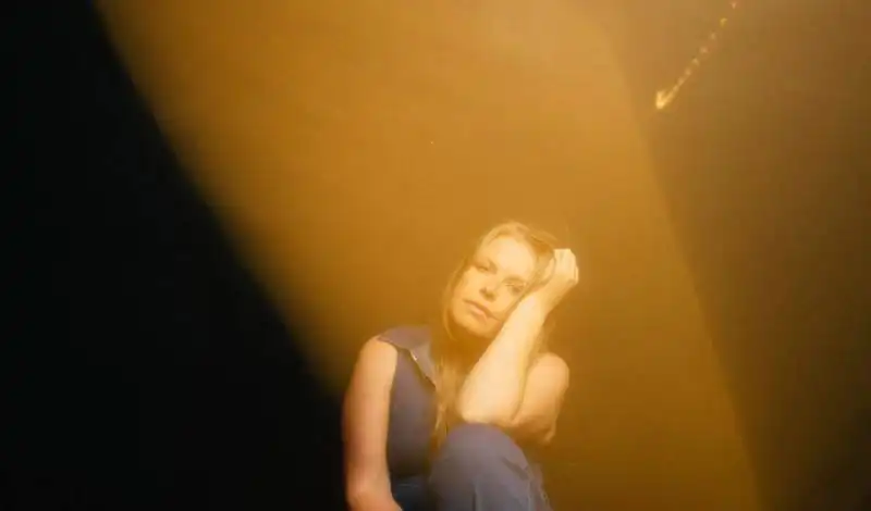 Image of a woman sitting alone in a dimly lit room with warm, moody lighting.