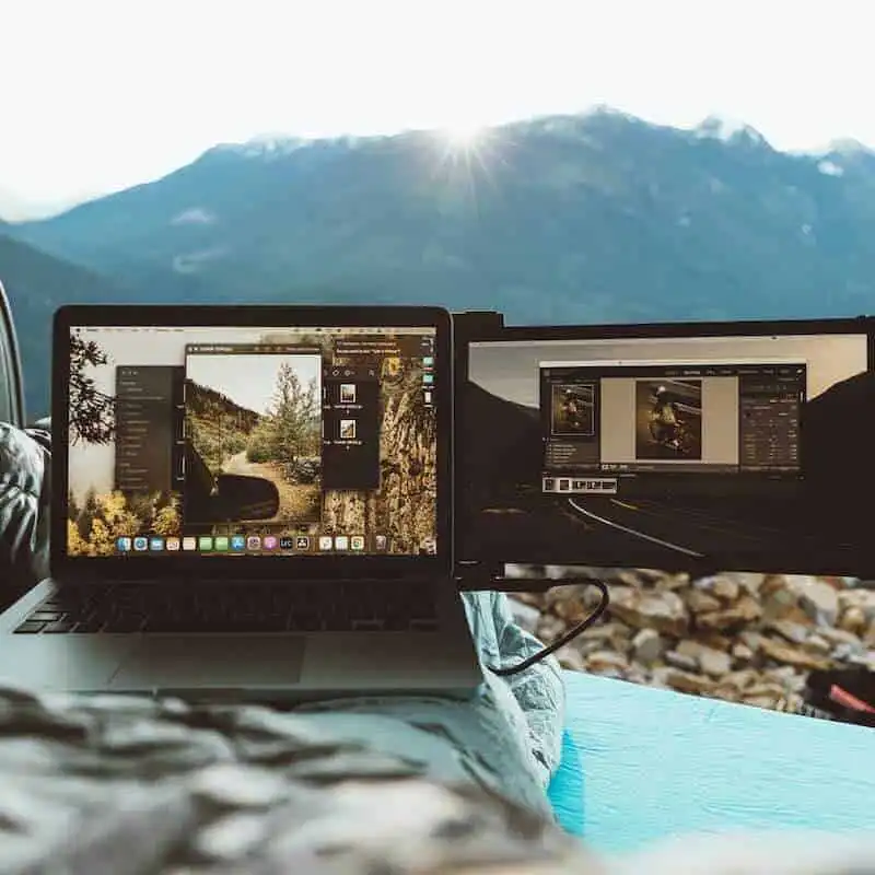 High-resolution photo of a laptop and external monitor set up in outdoor mountain scenery, ideal for digital nomads and content creators.