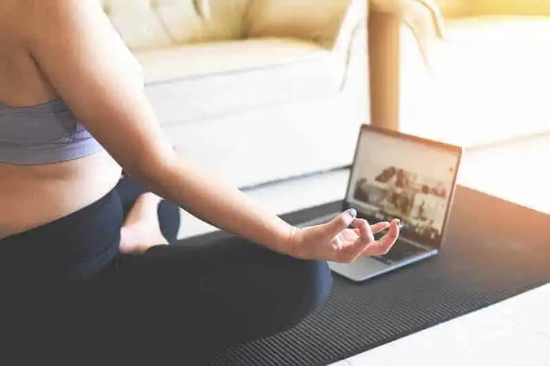 Relaxing person meditating with a laptop during yoga session at home.