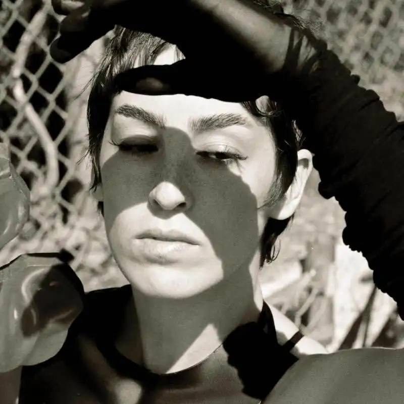 Close-up monochrome photo of a woman shielding her eyes with her hand, natural sunlight, outdoor setting.
