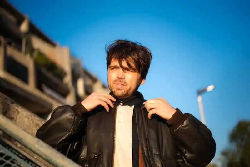 Male model adjusting jacket in urban setting, stylish streetwear, confident pose, natural light.